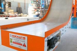 Close-up of an orange industrial magnetic conveyor with an entirely enclosed design, used for safely transporting drilling chips and ferromagnetic scrap.